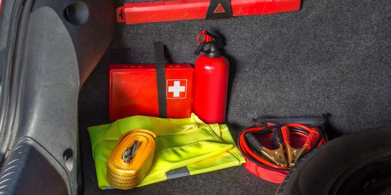 Interior of the trunk of the car in which there is a first aid kit, fire extinguisher, warning triangle, reflective vest, starter cables and tow rope